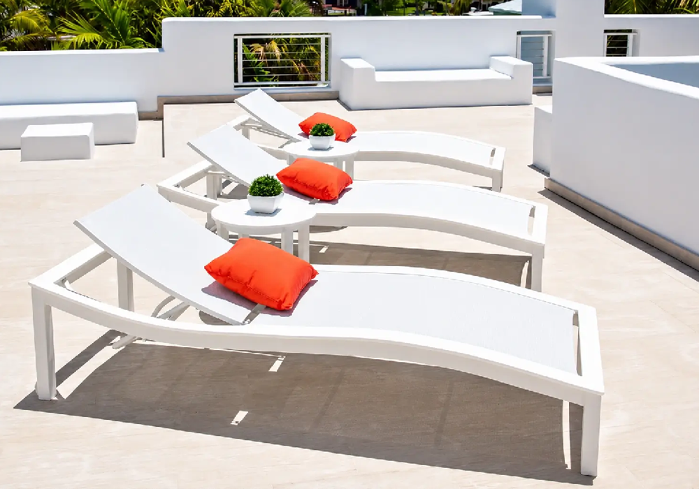 Modern curved chaise lounges with white frames and accent pillows creating a sophisticated luxury pool deck design.
